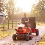 man driving ride on lawn mower with tow-behindy utility dump cart